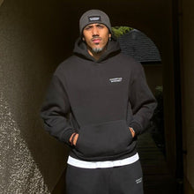 Load image into Gallery viewer, Person wearing a black hoodie and pants standing in an archway.