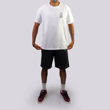 Load image into Gallery viewer, Man wearing a white t-shirt with a logo and black shorts on a light gray background
