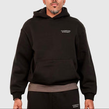 Load image into Gallery viewer, Man wearing a black Champion hoodie on a light gray background