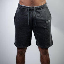 Load image into Gallery viewer, Person wearing dark gray shorts with a brand logo on a light gray background
