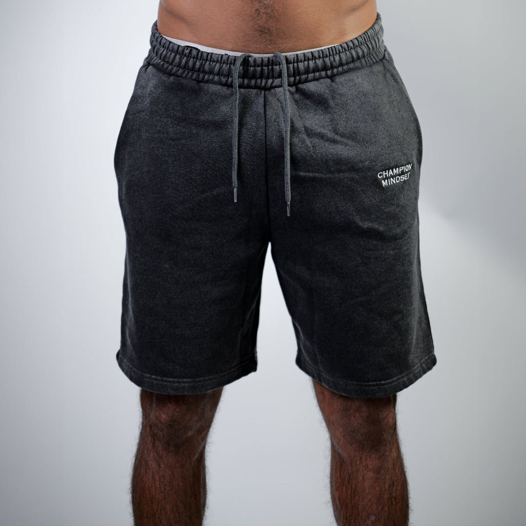 Person wearing dark gray shorts with a brand logo on a light gray background